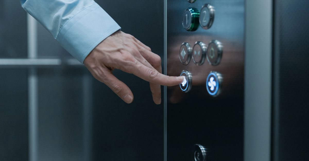 A person pressing an elevator button in a modern building, highlighting technology and urban life.